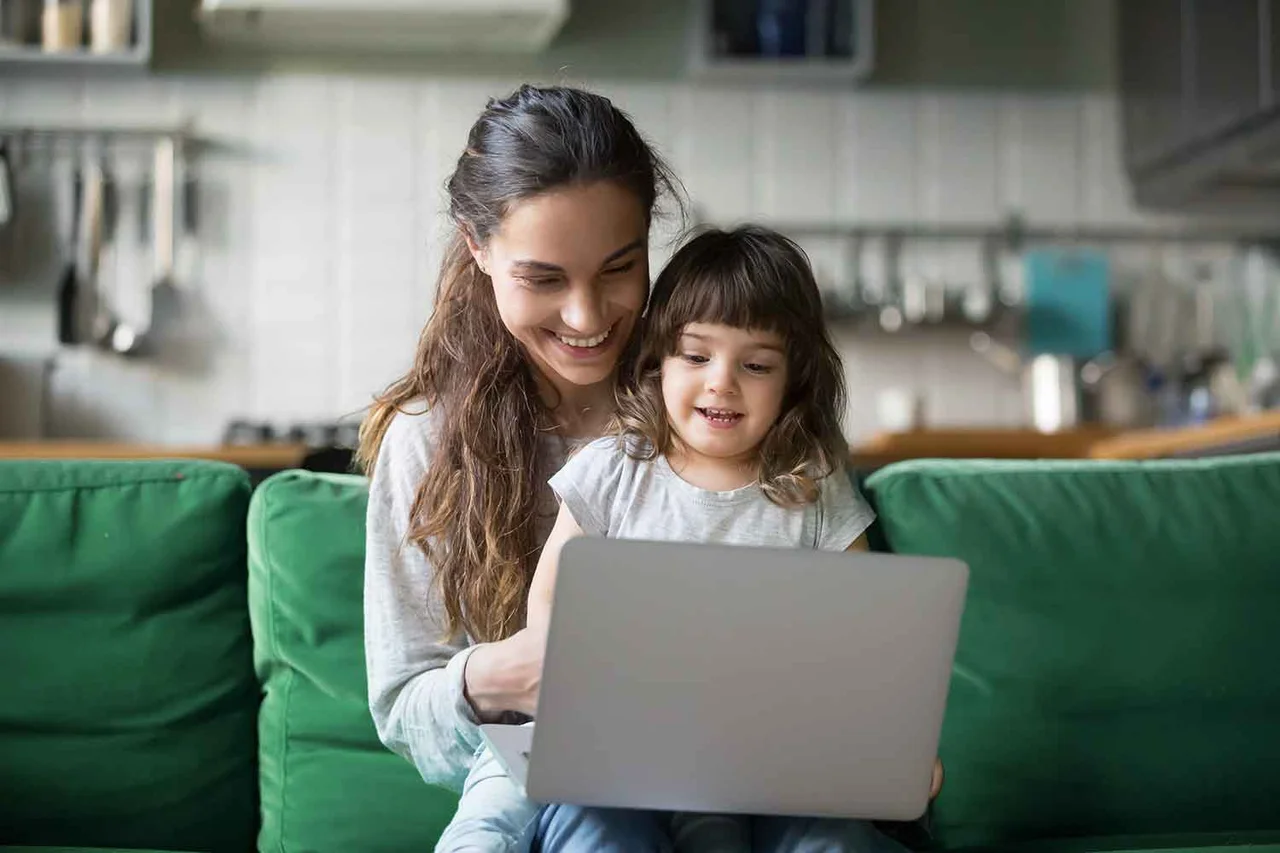 eine Frau und ein Kind sitzen auf einer Couch und schauen auf einen Laptop