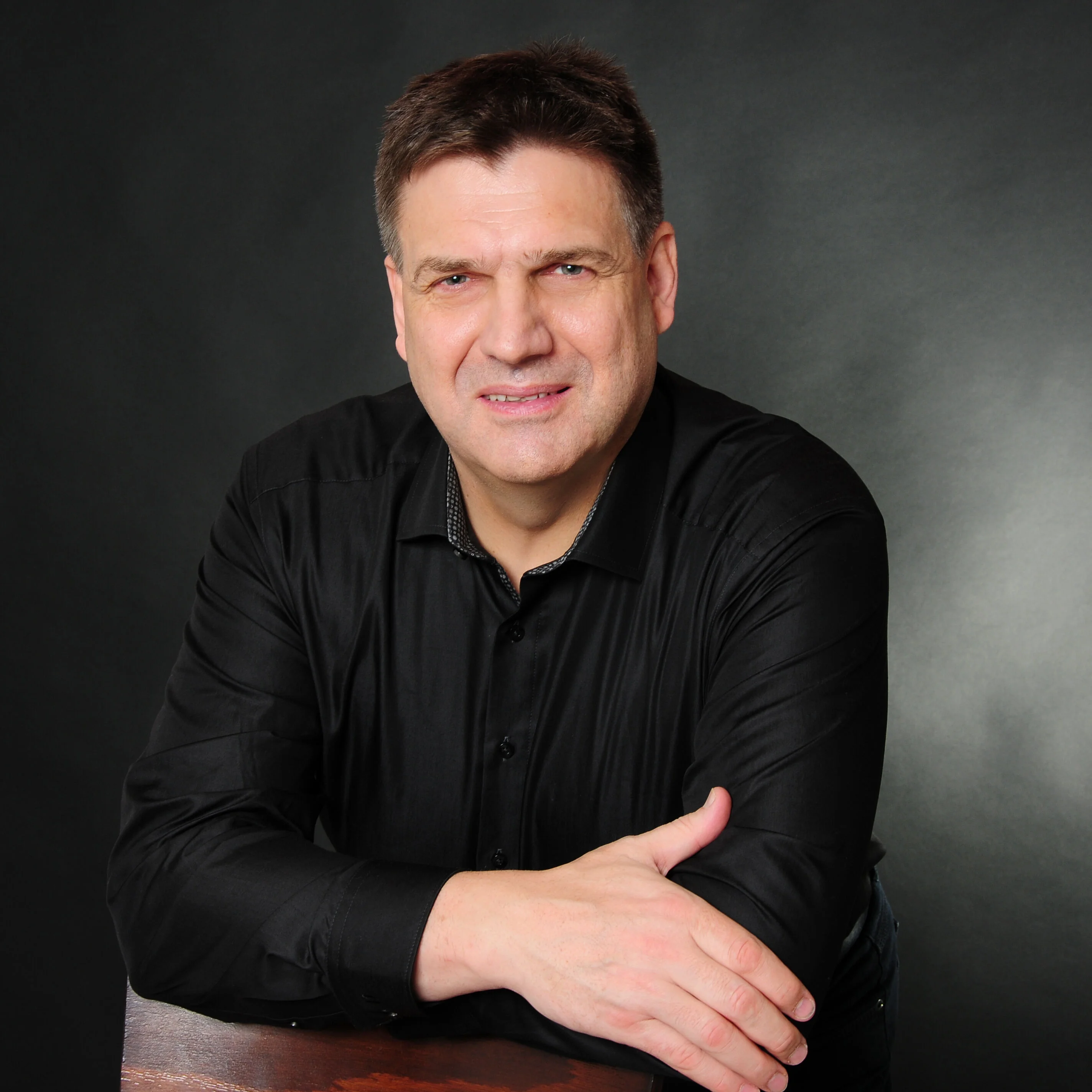 Professionelles Foto von Peter Jähne, Lernzeitbegleitung beim IBB, in dunklem Hemd vor dunklem Hintergrund.