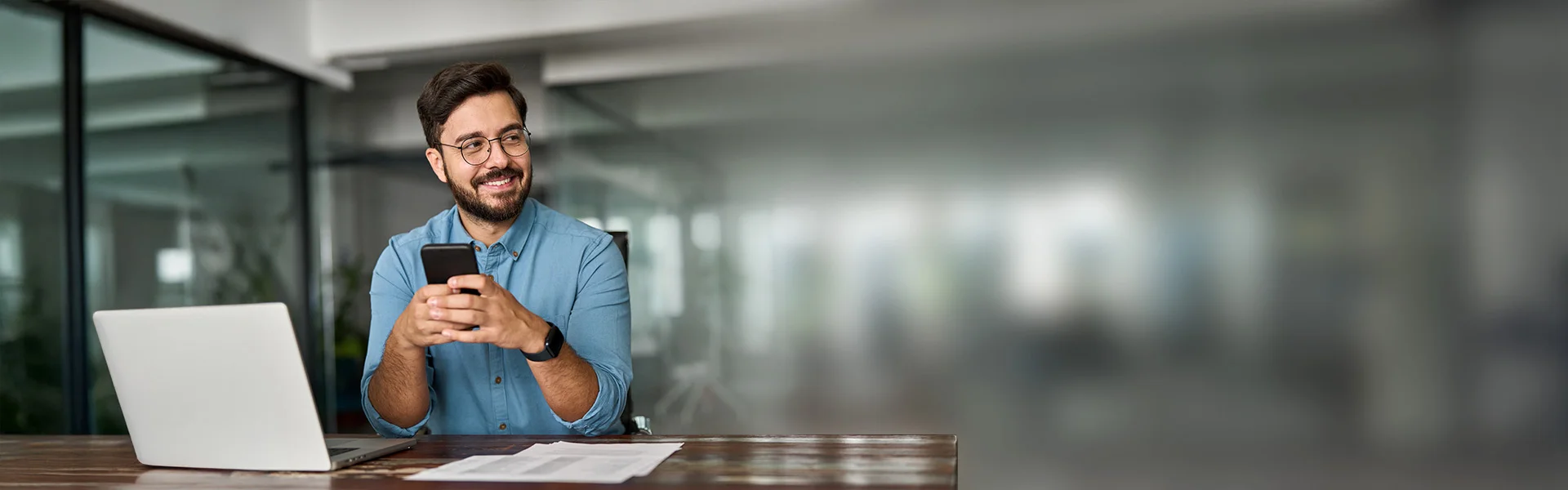 Mann in einem modernen Büro schaut konzentriert auf sein Smartphone.