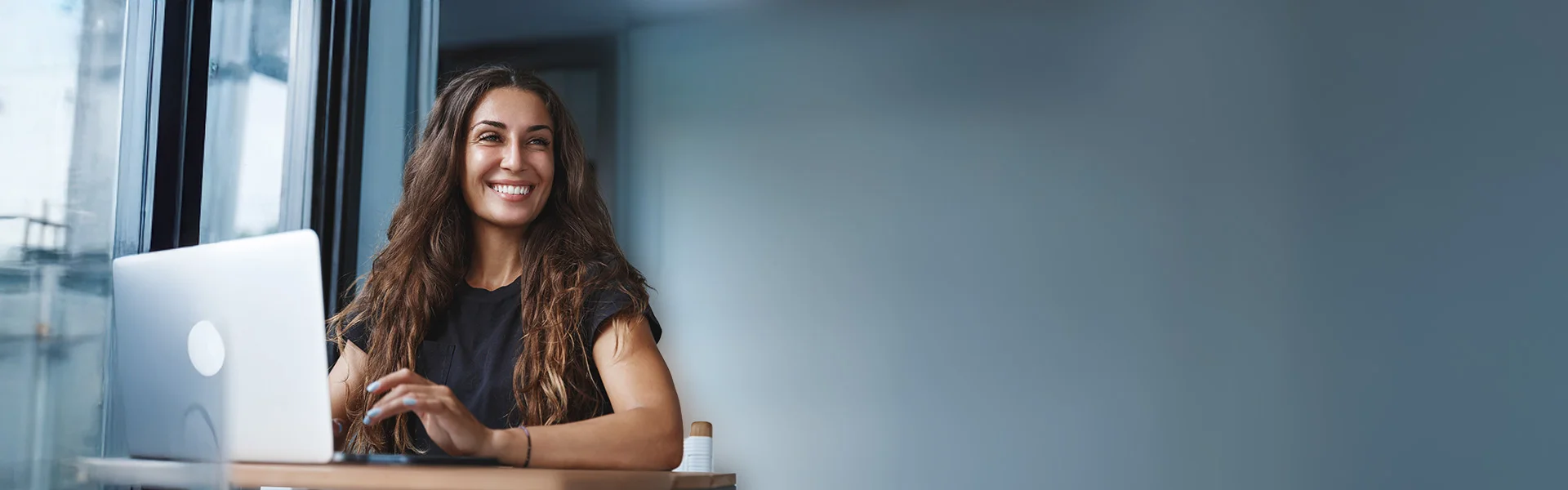 Junge Frau im Büro sitzt lächelnd vor ihrem Laptop