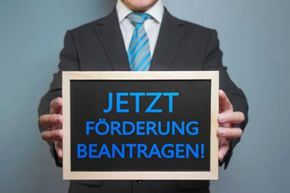ein Mann in einem Anzug mit einem Schild worauf steht Jetzt Förderung beantragen