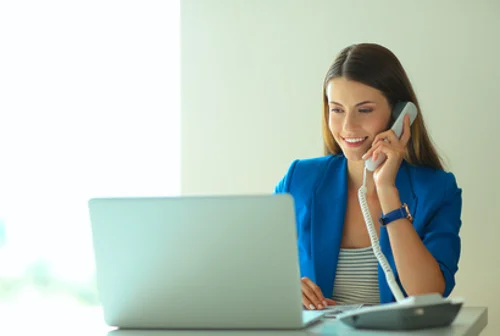 eine Frau, die an einem Schreibtisch mit Laptop und Telefon sitzt und telefoniert
