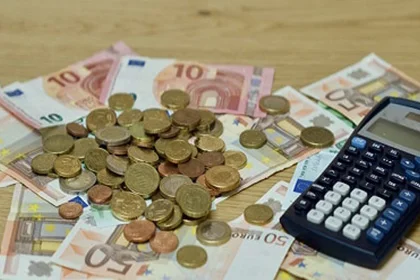 ein Haufen Geld in Scheinen und Münzen und ein Taschenrechner