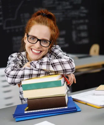 ein Mädchen sitzt an einem Schreibtisch mit Büchern und einer Tafel im Hintergrund