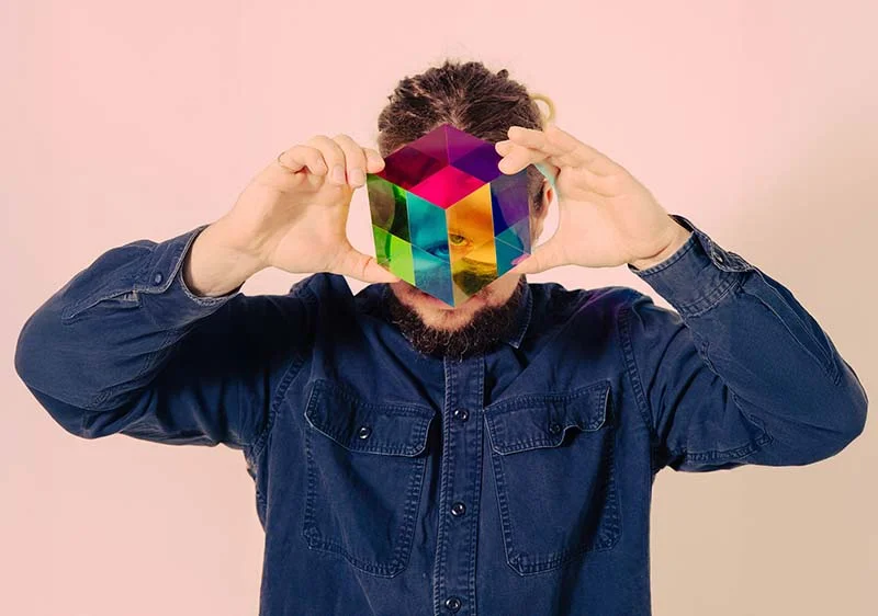 Mann hält einen verschiedenfarbigen Glaswürfel vor sein Gesicht.