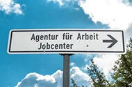 ein Schild mit einem Pfeil nach rechts darauf steht Agentur für Arbeit Jobcenter