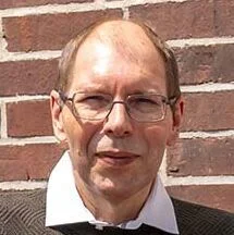 Der erfolgreiche Umschüler André Pardun steht mit verschränkten Armen vor einer geziegelten Hauswand.