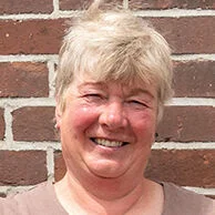 Die stolze Weiterbildungsteilnehmerin Astrid Estel steht, die Hände auf die Hüften gestützt, vor einer geziegelten Hauswand.