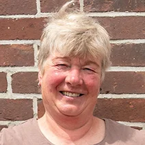 Die stolze Weiterbildungsteilnehmerin Astrid Estel steht, die Hände auf die Hüften gestützt, vor einer geziegelten Hauswand.