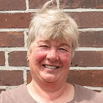 Die stolze Weiterbildungsteilnehmerin Astrid Estel steht, die Hände auf die Hüften gestützt, vor einer geziegelten Hauswand.