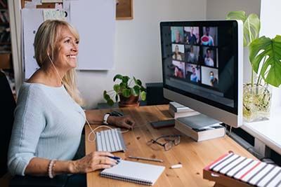 Frau mittleren Alters sitz am PC und hat eine Telekonferenz. Sie lächelt dabei und wirkt zufrieden